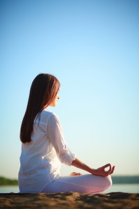 Side view of meditating woman sitting in pose of lotus against blue sky outdoors