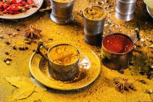 Set of spices pepper, turmeric, anise, coriander in vintage metal cups over yellow curry powder